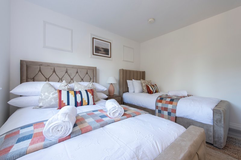 Bright bedroom with two double beds, upholstered headboards, white pillows and patterned throws