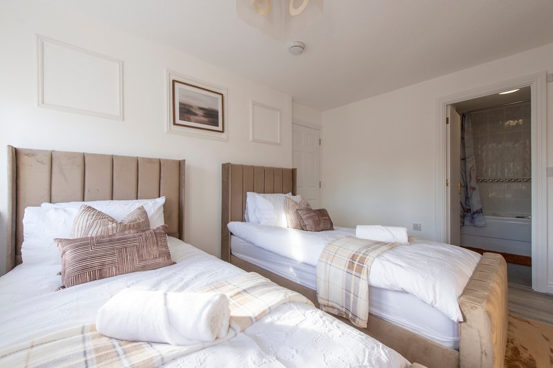 Bright bedroom with two single beds, upholstered headboards, white bedding and wooden flooring