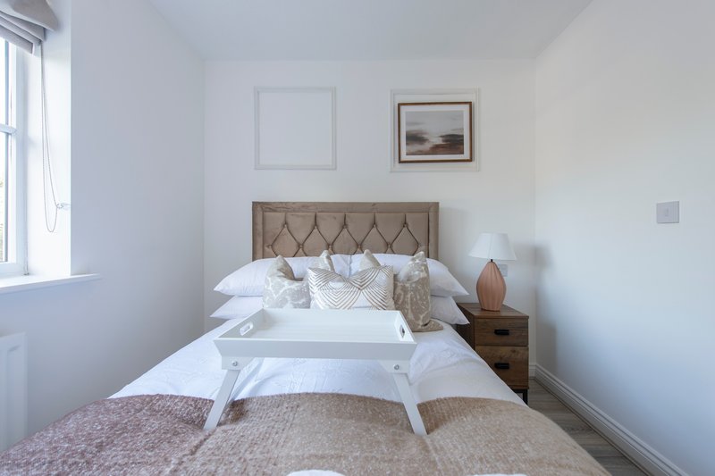 Bright bedroom with double bed, upholstered headboard, wooden nightstand, and framed landscape artwork