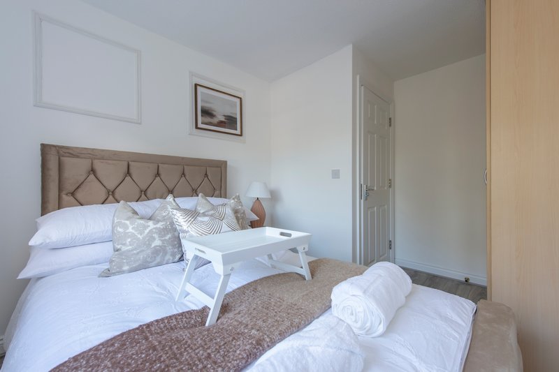 Bright bedroom with upholstered headboard, white bedding, and small white bench at foot of bed