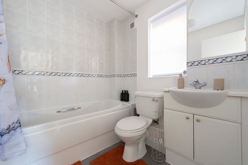 Clean modern bathroom with white tiles, bathtub, toilet, sink and window