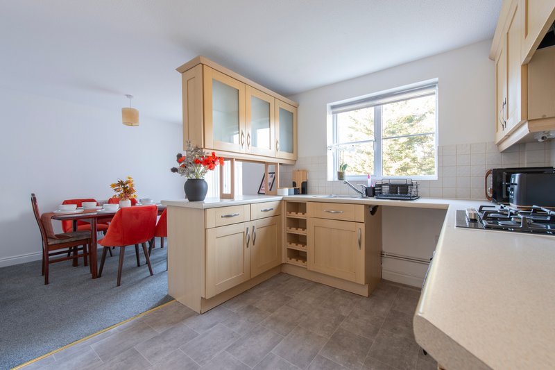 Modern kitchen with wooden cabinets, dining area with red chairs and table, bright window