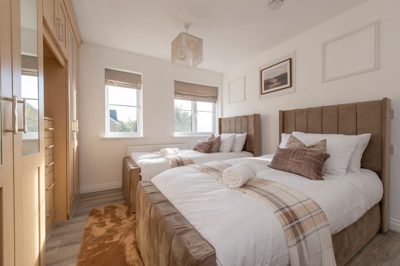 Bright twin bedroom with two double beds, brown upholstered headboards, white bedding and windows
