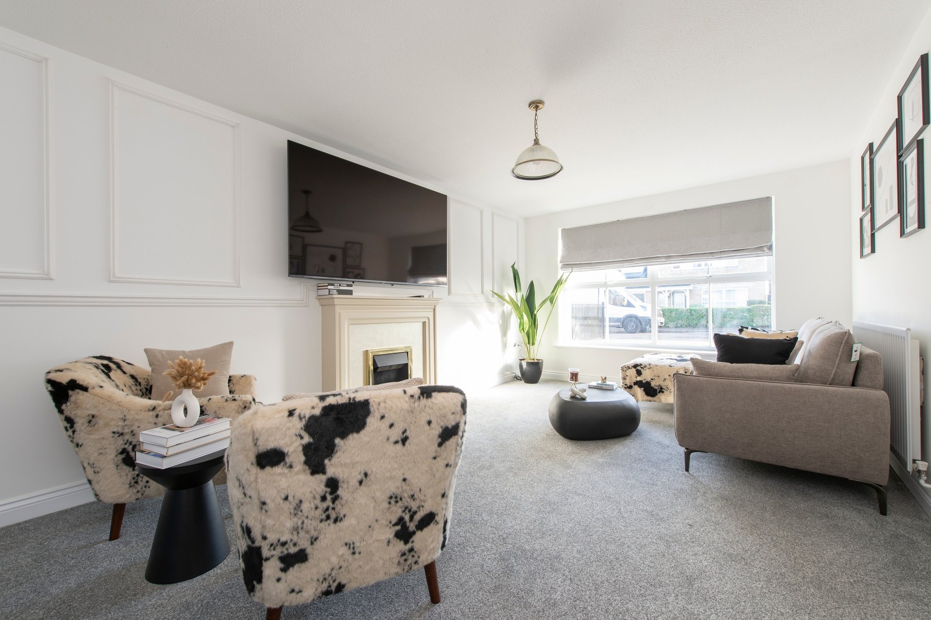 Modern living room with cream armchair, sofa, fireplace, wall-mounted TV and large windows