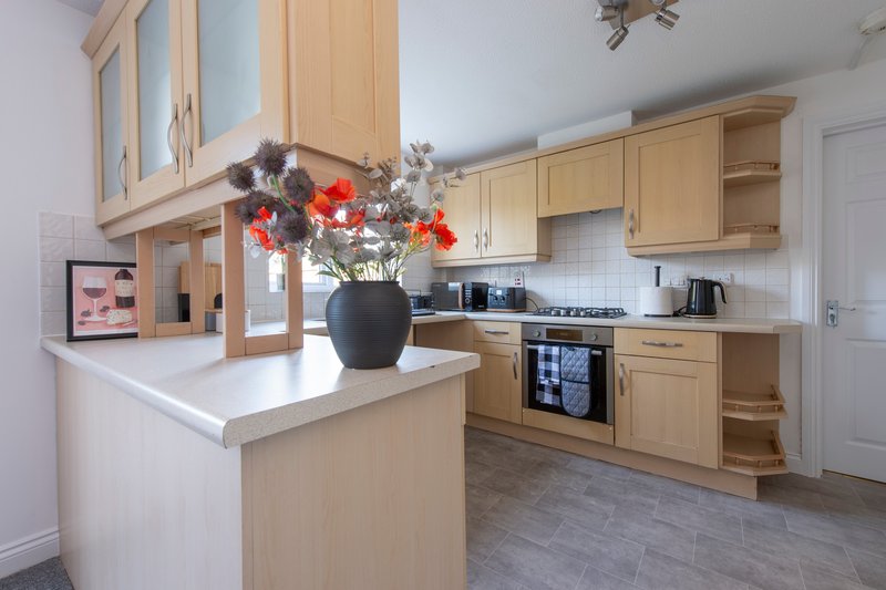 Modern kitchen with wooden cabinets, white countertops, island, and red flower arrangement