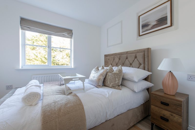 Bright bedroom with double bed, upholstered headboard, wooden nightstand and window