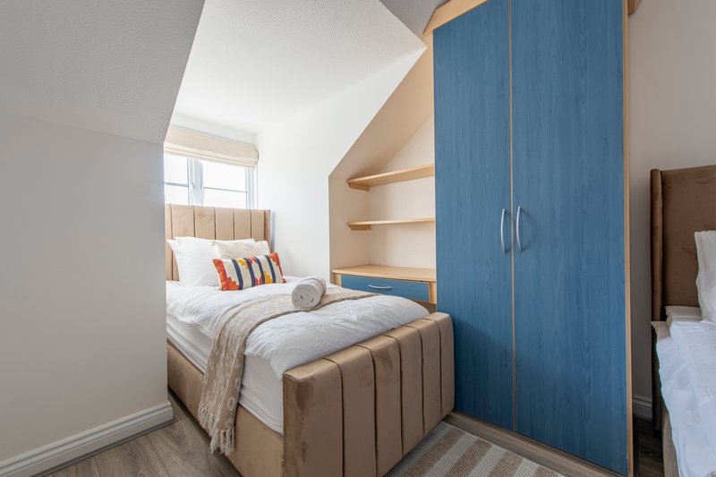 Modern bedroom with double bed, blue wardrobe, shelving and natural light from window