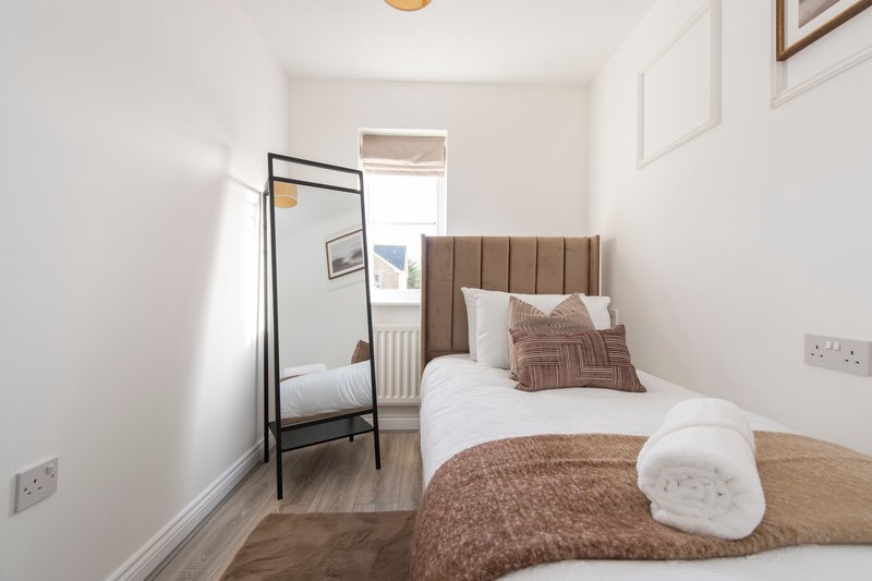 Compact bedroom with single bed, upholstered headboard, mirror and window
