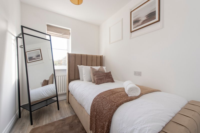Modern bedroom with double bed, brown headboard, standing mirror and framed wall art
