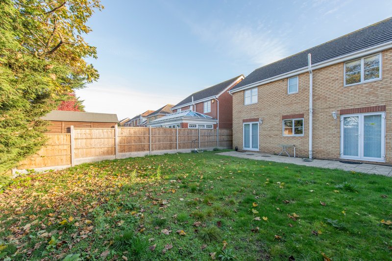 Rear garden view of brick detached house with lawn, wooden fence and patio area