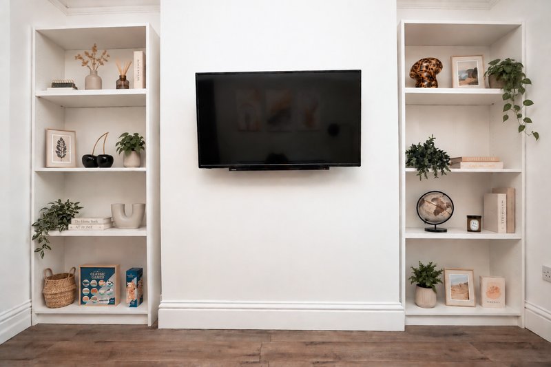 Modern living room with wall-mounted TV, white built-in shelving units with plants and decor