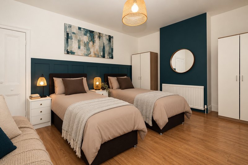 Twin bedroom with teal accent wall, two beds, wooden floor, and modern decor