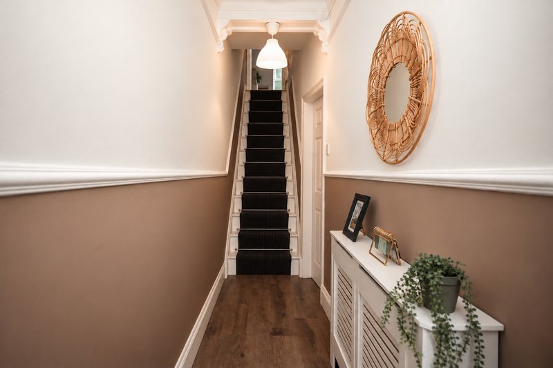 Hallway with staircase, woven circular wall decoration, radiator and potted plant