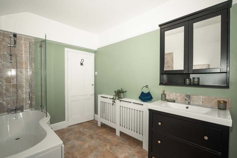 Modern bathroom with sage green walls, black vanity, white bathtub and shower enclosure