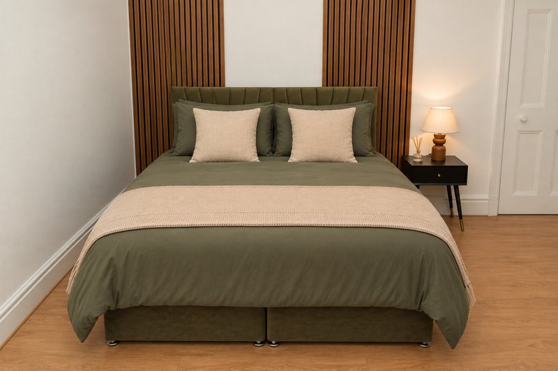 Modern bedroom with olive green bedding, cream pillows, wooden floor, and bedside lamp