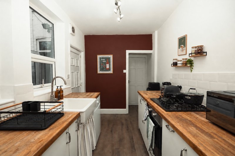Galley kitchen with wooden countertops, white cabinetry, burgundy accent wall and stainless steel appliances