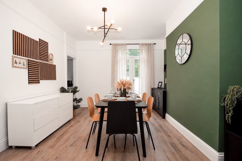 Dining room with black table, orange chairs, green accent wall and wooden flooring