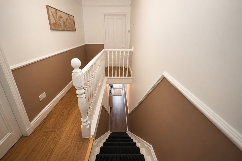 Staircase with white bannister, wooden floor, and two-tone brown and white walls
