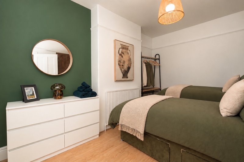 Bedroom with green accent wall, white dresser, round mirror, wooden floor and green bed
