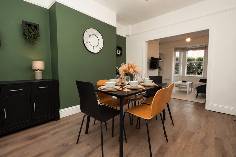 Dining room with green walls, wooden table, mixed seating, and open-plan kitchen view