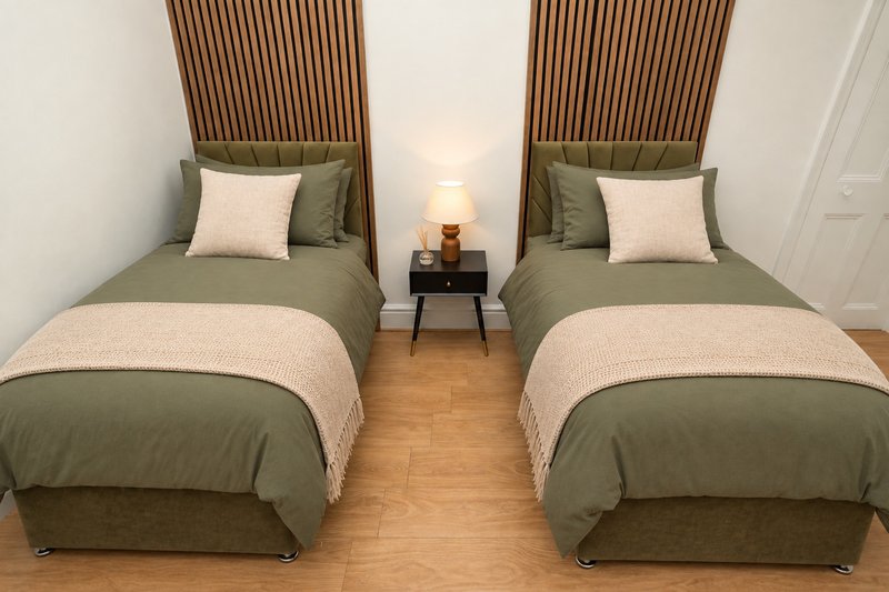 Twin bedroom with two beds, green bedding, wooden headboards and bedside lamp