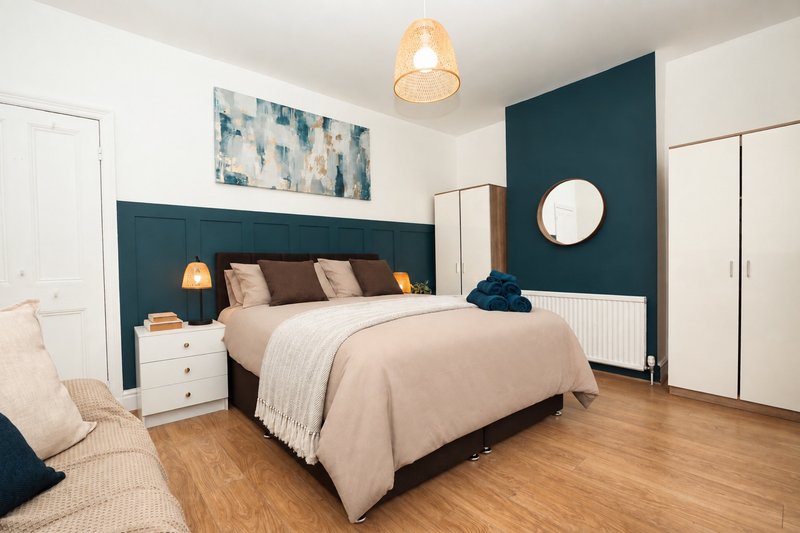 Modern bedroom with dark teal headboard, double bed, wooden floor and pendant lighting