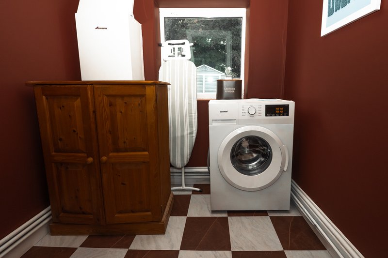 Laundry room with washing machine, wooden wardrobe, ironing board and red walls