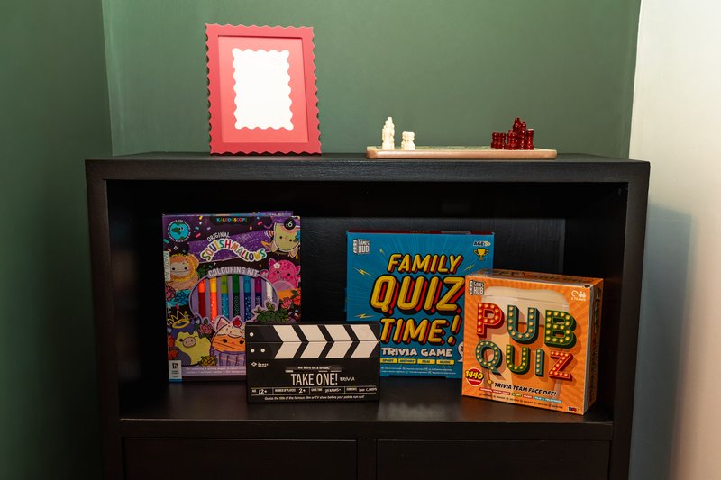 Black shelving unit with board games, decorative frame, and small ornaments against green wall