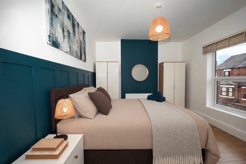 Modern bedroom with teal panelled headboard, double bed, woven pendant light, and street view window