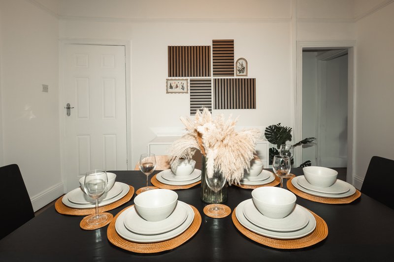 Dining table set with white place settings, orange chargers, glassware, and pampas grass centerpiece