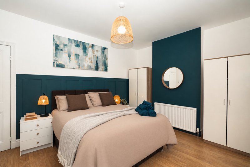 Modern bedroom with double bed, teal headboard, white nightstands, pendant light, and round mirror