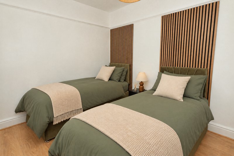 Bedroom with two single beds, green bedding, wooden headboards and hardwood floor
