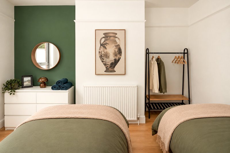 Bedroom with two beds, green accent wall, round mirror, framed artwork, and clothing rack