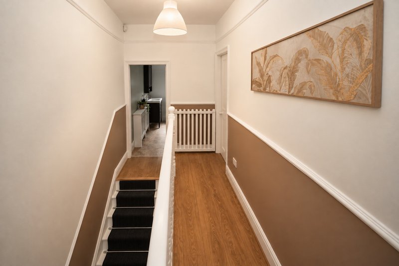 Narrow hallway with wooden floor, staircase, radiator, and framed wall art