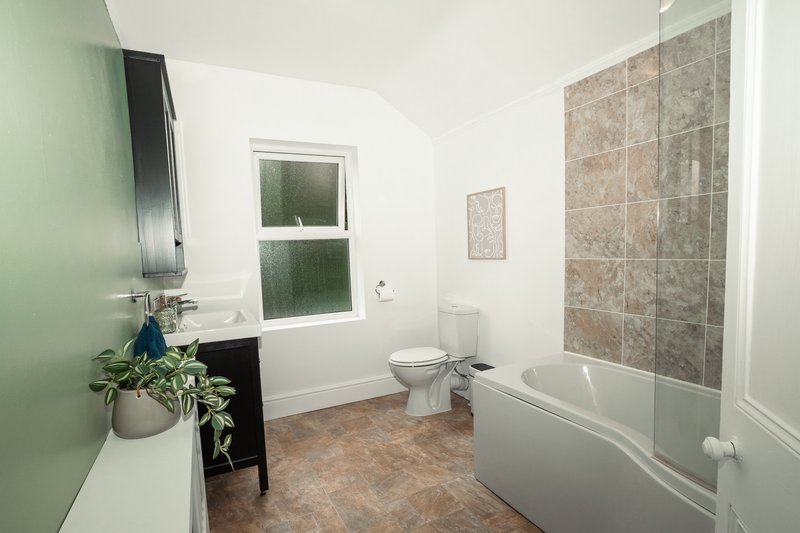 Modern bathroom with bathtub, toilet, sink, window and green feature wall