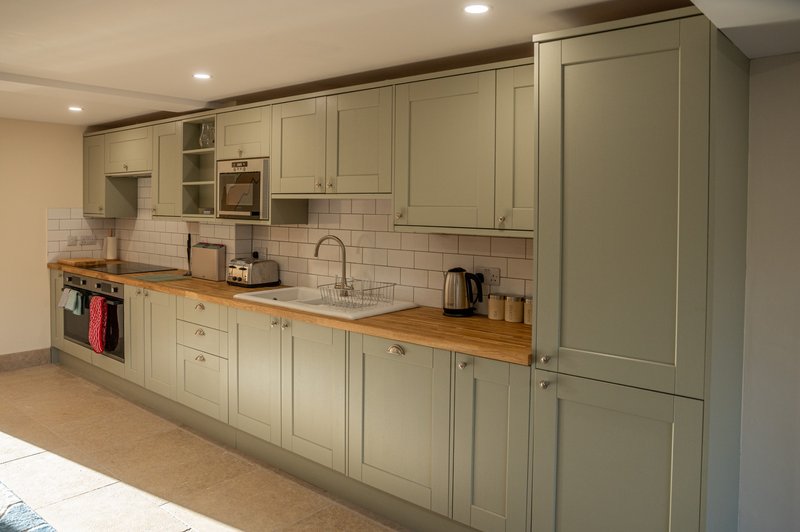 Modern kitchen with sage-green cabinetry, wooden countertop, white subway tile backsplash and stainless steel appliances