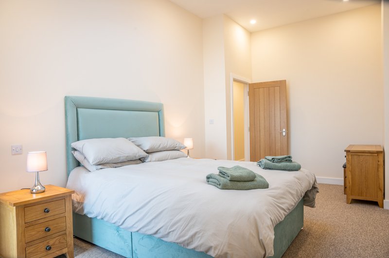 Bedroom with turquoise upholstered bed, white bedding, wooden nightstand and wardrobe
