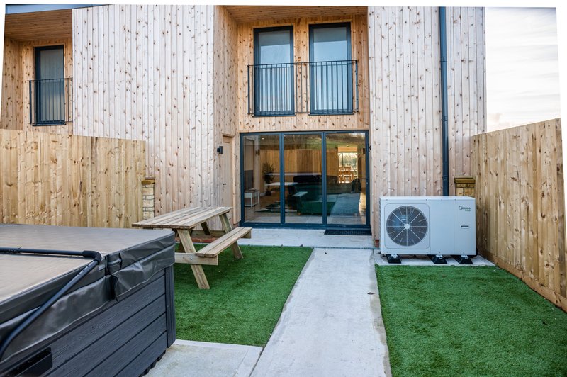 Modern residential courtyard with artificial grass, wooden seating, heat pump, and glass doors