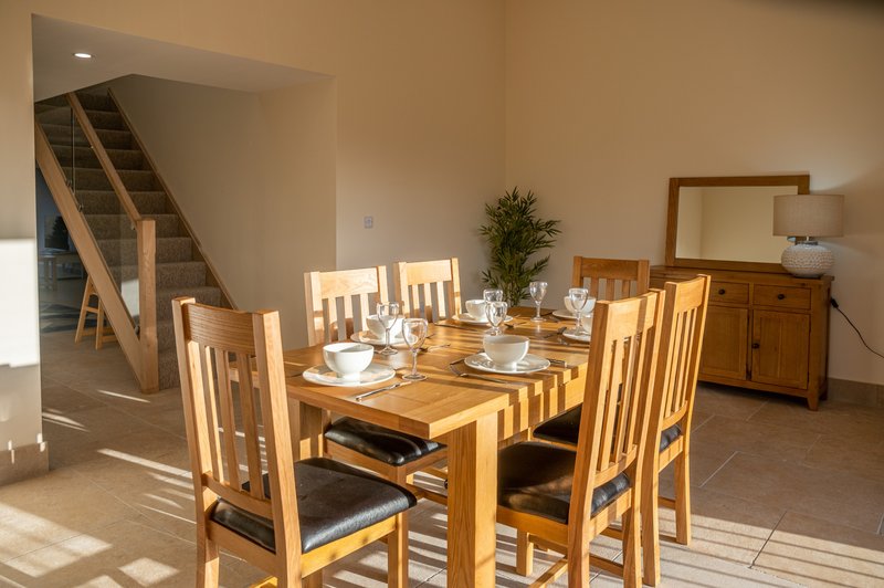 Bright dining room with wooden table, four chairs, staircase and mirror visible