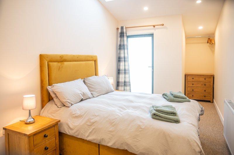 Bright bedroom with mustard yellow upholstered bed, white bedding, wooden nightstand and dresser