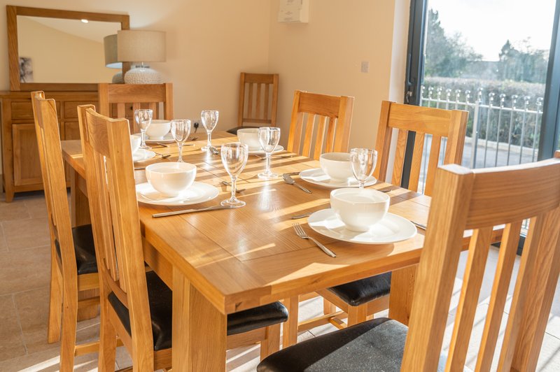 Dining room with wooden table, chairs, place settings, and large windows overlooking trees