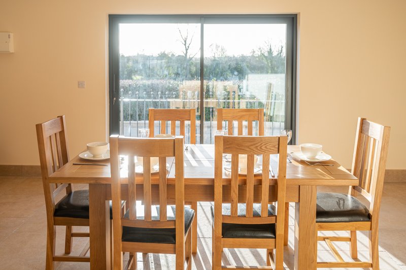 Dining room with wooden table, four chairs, place settings, and glass doors overlooking balcony and landscape