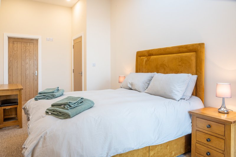 Bright bedroom with mustard velvet headboard, white bedding, folded towels, and wooden furniture