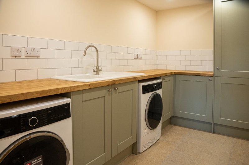Utility room with two washing machines, wooden countertop, sage cabinetry and subway tile wall
