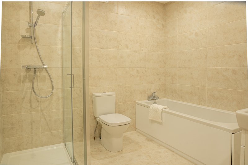 Clean bathroom with shower cubicle, toilet, and bathtub with beige tile walls