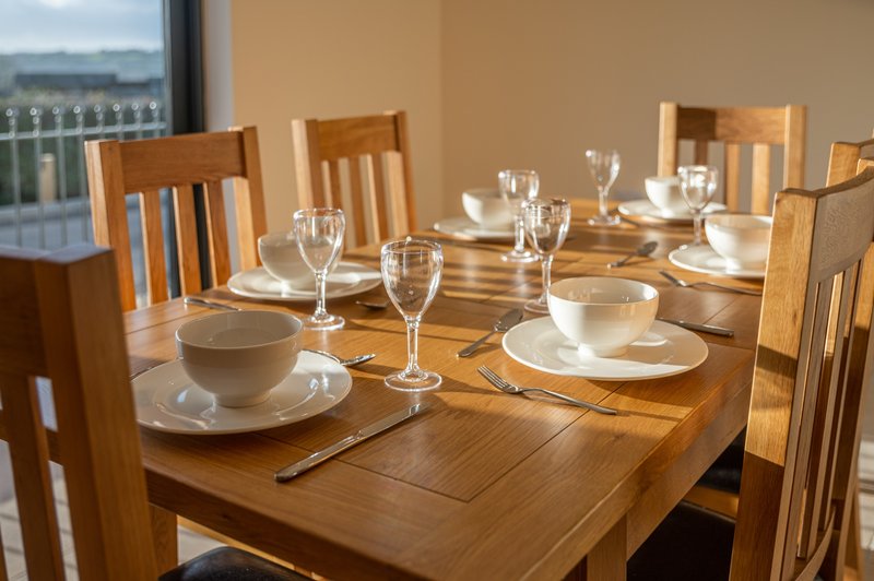 Wooden dining table set for meal with place settings, glasses, and chairs