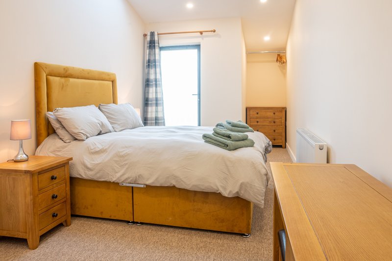 Bright bedroom with yellow upholstered bed, wooden furniture, and window with blue curtains