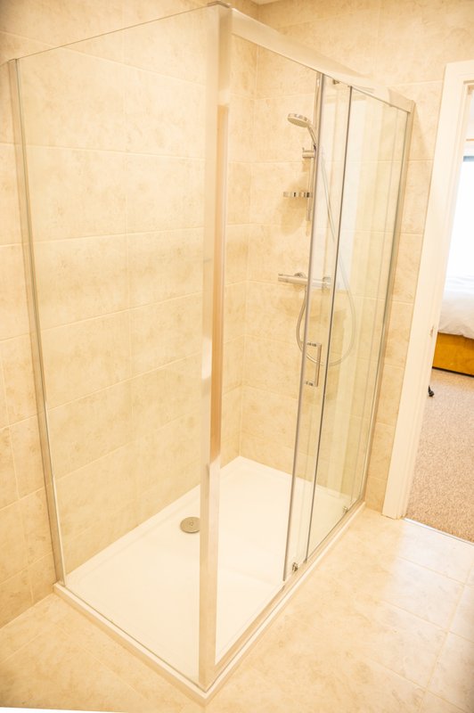 Modern bathroom with corner shower cubicle, glass doors and beige tile walls