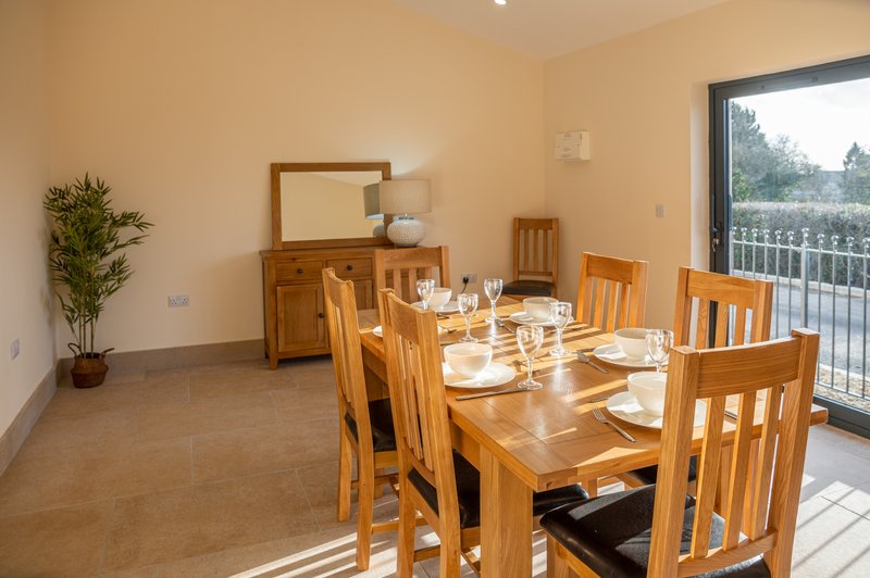 Dining room with wooden table, chairs, potted plant and garden view through glass doors
