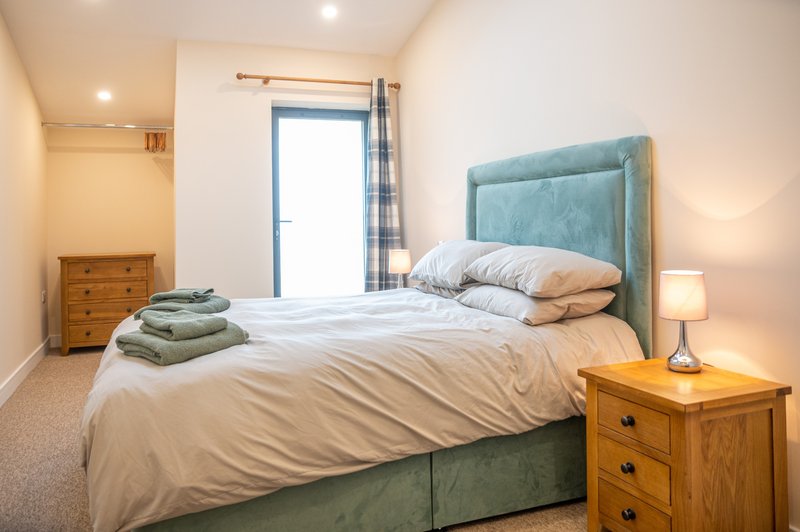 Bright bedroom with teal upholstered bed, white bedding, wooden nightstand, and blue curtains